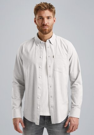 Weißes Hemd mit Knöpfen aus strukturiertem Stoff, ausgestattet mit einer Brusttasche und einem geraden Saum, über einem weißen T-Shirt getragen und kombiniert mit grauen Jeans.