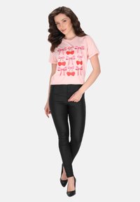 Tricou scurt cu mânecă scurtă de un roz deschis, cu cireșe roșii și fundițe roz. Asortat cu pantaloni negri, mulați și tocuri negre. Textură netedă.