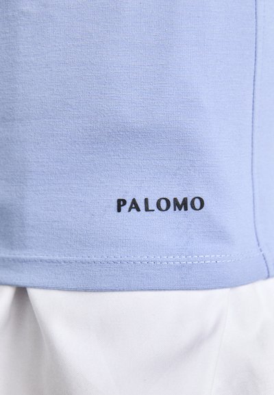 Light blue cotton shirt with white fabric underneath, featuring a stitched hem and the word "PALOMO" in black on the lower side.