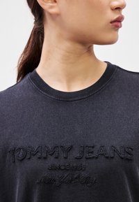 Tricou negru din bumbac, cu text brodat „TOMMY JEANS”, cu textură netedă și decolteu rotund.