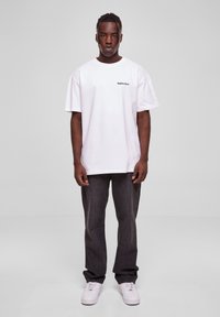Hvit bomull T-skjorte med "forgotten" trykket på venstre bryst, sammen med mørkegrå jeans og hvite sneakers. Standard passform, rund hals.