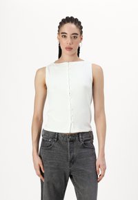 Haut blanc à rayures, sans manches, avec un décolleté carré et une patte de boutonnage à l'avant, associé à un jean gris taille haute.