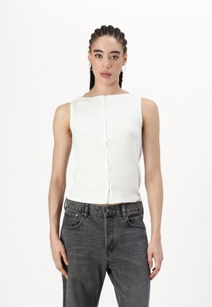 Haut blanc à rayures, sans manches, avec un décolleté carré et une patte de boutonnage à l'avant, associé à un jean gris taille haute.