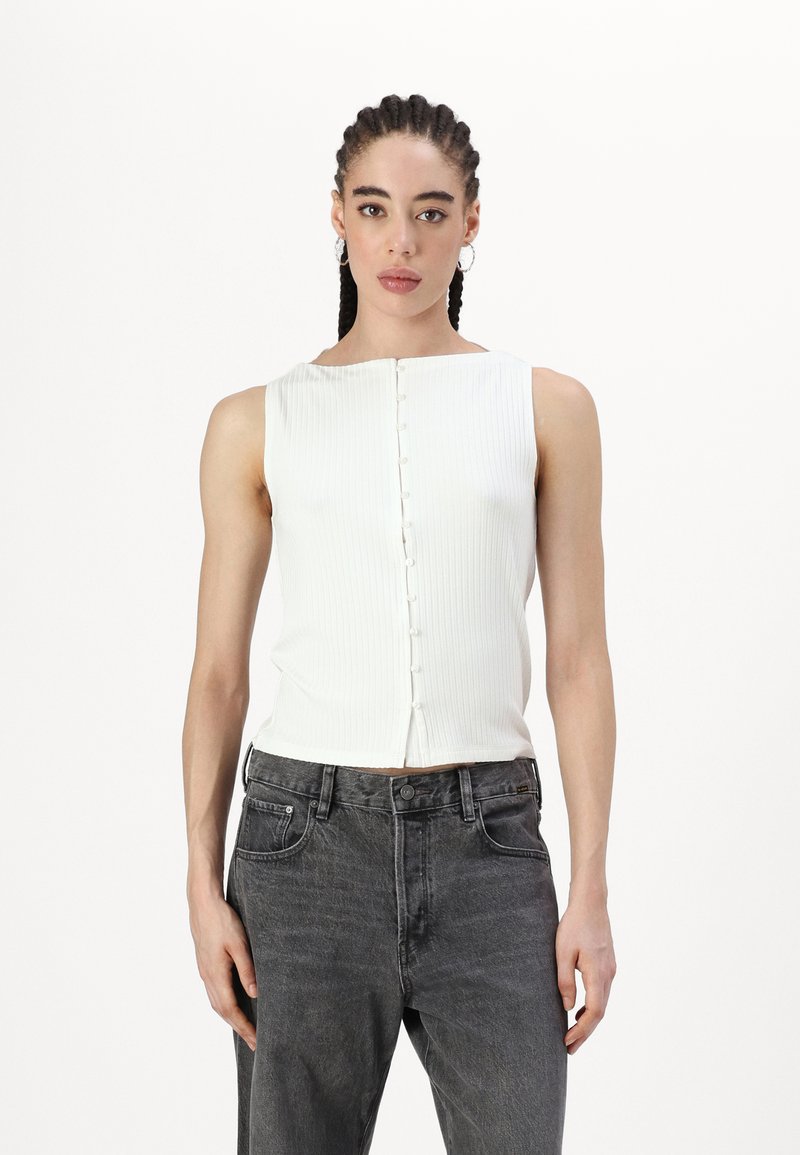 Haut blanc à rayures, sans manches, avec un décolleté carré et une patte de boutonnage à l'avant, associé à un jean gris taille haute.