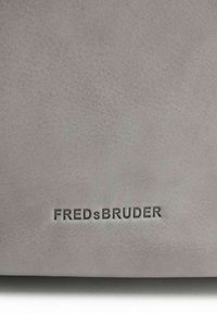 Grijze leren tas met een gestructureerd oppervlak. Het logo "FREDsBRUDER" is op de voorkant geperst. Eenvoudig, modern ontwerp.