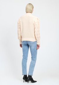 Maglione lavorato a maglia rosa chiaro con maniche floreali testurizzate, orlo a coste, abbinato a jeans azzurri chiari e stivaletti neri con tacco.
