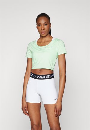 Gaiši zaļa sporta topa blūze ar īsām piedurknēm, kombinēta ar baltām šortiem, kuriem ir melns "NIKE PRO" jostasvieds un logo.