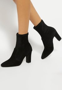 Black suede ankle boots with a pointed toe and a block heel. They feature a fitted collar and seam detailing along the sides.