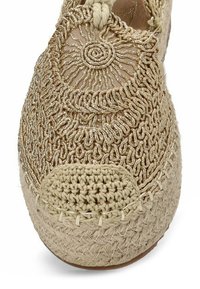 Zapato de esparto beige de crochet con parte superior de tejido texturizado, detalle bordado circular y punta reforzada de tejido.