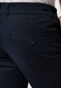 Námořnické modré kalhoty vyrobené z bavlny, s kapsou vzadu na knoflík a jemnými stehy podél švů.