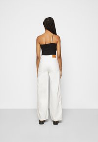 Top preto de um ombro só combinado com calças brancas de cintura alta e perna larga, e sapatos de plataforma pretos. Detalhe em couro notável na cintura.