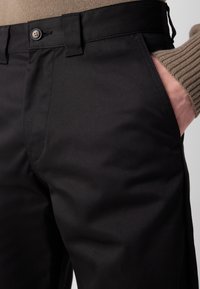 Sorte bomuldstrusser med en glat overflade, frontlommer og en klassisk knaplukning i livet. Subtile, skarpe design detaljer.