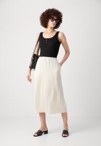 Top sin mangas negro con detalles de botones, combinado con una falda midi blanca fluida. Sandalias negras de deslizamiento y un bolso negro completan el look.