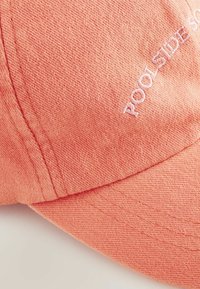Gorra de béisbol color coral con tela texturizada, que presenta el texto bordado "POOLSIDE SOCIETY" en la parte frontal, visera curva y costuras cosidas.