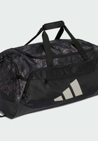 Bolsa deportiva negra con un patrón texturizado en púrpura, asas dobles, bolsillos con cremallera y un gran logo beige de Adidas en un lado.
