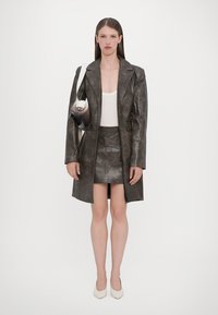 Dark leather trench coat over a white top and a grey mini skirt. Pale stilettos and a handbag with a strap. Smooth texture, long sleeves.