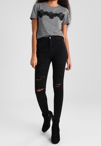 Szara krótka koszulka z krótkim rękawem z czarnym koronkowym wykończeniem przy dekolcie, zestawiona z czarnymi podartymi rurkami i czarnymi botkami za kostkę.