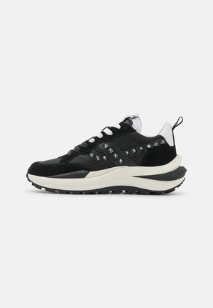 Czarno-biały sneaker z grubą podeszwą, białymi sznurowadłami, metalowymi ćwiekami po bokach i pętelką na pięcie z tyłu, widziany z boku.