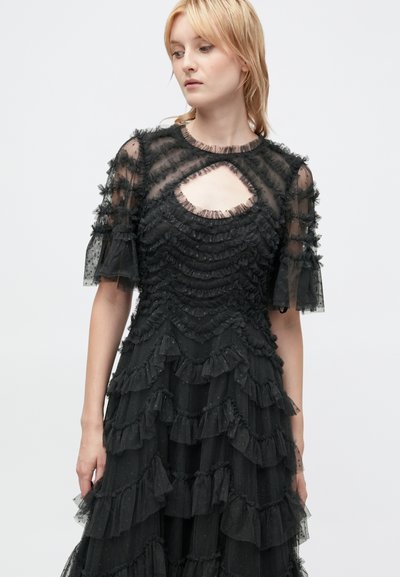 Czarna sukienka z warstwowymi falbanami, przezroczystymi krótkimi rękawami i dekoltem w kształcie łezki. Teksturowany materiał dodaje głębi do projektu.