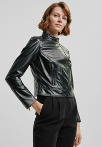 Czarna skórzana kurtka z wysokim kołnierzem i zapinanymi na zamek kieszeniami. Posiada dopasowany krój oraz gładką, błyszczącą teksturę.