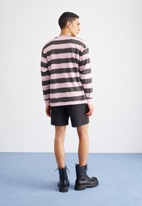 Camisa de manga larga a rayas en colores rosa y negro, combinada con pantalones cortos negros. El modelo lleva botas negras con cordones y suela gruesa.