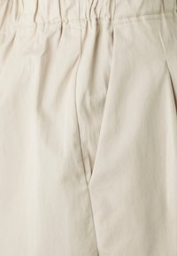 Tessuto di cotone beige con una superficie liscia, caratterizzato da dettagli plissettati e una vita arricciata. La vista ravvicinata mette in evidenza il materiale e il design.