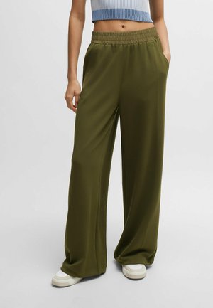 Olive green wide-leg pants with an elastic waist, soft fabric, and side pockets. Paired with white sneakers, styled for comfort.