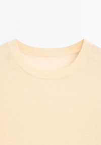 Helle beigefarbene Baumwoll-T-Shirt mit rundem, geripptem Hals, glatter Textur und kurzen Ärmeln. Der Stoff wirkt weich und leicht.