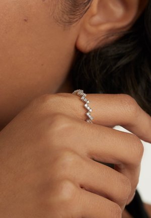 Silver zigzag ring set with small clear stones, showcasing a delicate and textured design on a hand with a natural skin tone.