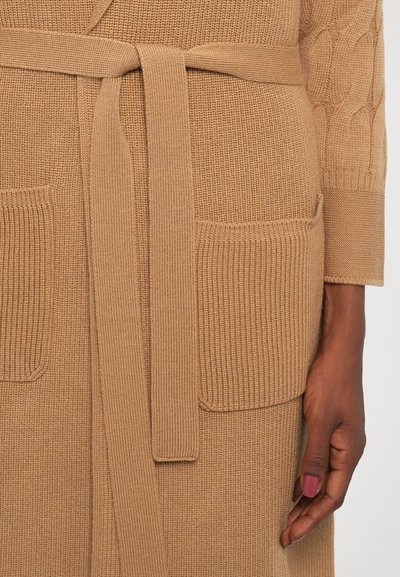 Καφέ πλεχτό κάρντιγκαν με ραμμένες τσέπες, αντίστοιχο ζωνάκι και υφή στα μανίκια. Λείο φινίρισμα, μεσαίου πάχους.