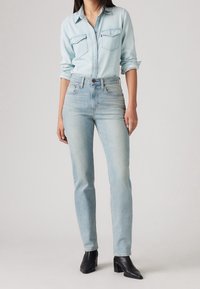 Ljusblå denimskjorta med två bröstfickor och knappstängning; matchad med ljusblå slim-fit jeans och svarta klackade anklarboots.