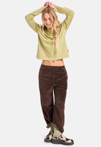 Cropped top verde a maniche lunghe, pantaloni in corduroy marroni e scarpe con motivo. Vestibilità ampia con una texture morbida e design rilassato per il massimo comfort.