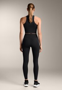 Haut de sport noir à encolure dos nu associé à un legging noir taille haute. Matériau texturé et coupe ajustée. Convient pour les entraînements.