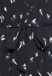 Czarna sukienka w białe i niebieskie kwiatowe wzory, z zapięciem na guziki z przodu oraz wiązanym paskiem w talii z tego samego materiału. Miękka tekstura.