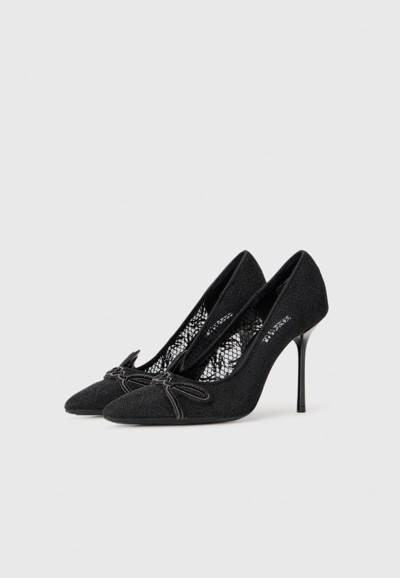 Schwarze High-Heels mit Spitze, spitzem Fuß und dekorativem Bogen an der Vorderseite. Glattes, elegantes, strukturiertes Material.