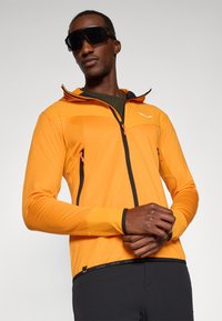 Πορτοκαλί ελαφρύ μπουφάν με κουκούλα, μαύρο φερμουάρ και δύο φερμουάρ τσέπες. Διαθέτει μαύρες λεπτομέρειες και εφαρμοστό σχέδιο.