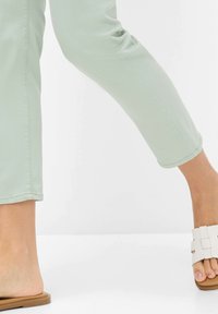 Pantaloni aderenti verde chiaro con una texture liscia, abbinati a sandali bianchi con dettagli squadrati e una suola di tonalità naturale.