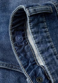 Jeans ovratnik jakne, s čvrstom teksturom, klasične plave boje, kontrastnom krem podstavljanjem i malim plastičnim detaljem dugmeta.