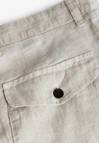Tissu en lin beige clair avec une surface texturée ; possède une poche arrière et un bouton sombre attaché au rabat de la poche.