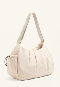 Beige fabric shoulder bag with adjustable strap, soft pleated design, and a small side pocket with a drawstring cord.