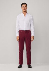Witte lange mouwen overhemd met knoopsluiting, gecombineerd met donker bordeauxkleurige broek, voorzien van zakken en een rechte snit. Zwarte schoenen maken de outfit compleet.