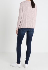 Pullover rosa chiaro, con texture, a maniche lunghe, abbinato a jeans skinny blu scuro e sneakers bianche, visto da dietro.