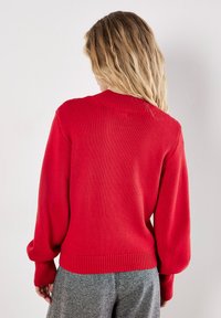 Czerwony sweter z dzianiny z prążkowanym kołnierzem, długimi rękawami w kształcie balonu i dopasowanym dołem. Pokazany z tyłu na neutralnym tle.