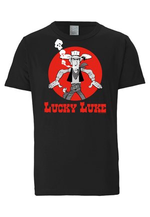 Sort bomulds t-shirt med en tegneseriefigur i en rød cirkel, der ryger med kranium detaljer. Teksten lyder "LUCKY LUKE" i fede røde bogstaver.