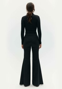 Schwarzes enges Langarmoberteil kombiniert mit hochtaillierten schwarzen, ausgestellten Hosen. Glatter Stoff mit minimalistischem Design und ohne sichtbare Muster.