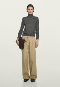 Maglione grigio a collo alto, materiale leggero, aderente ai polsi. Pantaloni beige a gamba larga, tessuto strutturato, vita alta. Borsa in suede marrone.