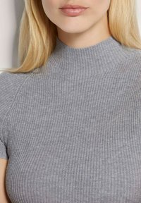Grijze geribbelde top met een hoge hals en korte mouwen, gemaakt van een rekbare stof die zich vormt naar de lichaamsvorm en de textuur accentueert.