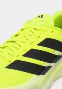 Bright yellow athletic shoe with black accents, textured mesh upper, and distinct three-stripe logo design. Laces are tightly secured.