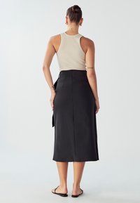 Črna, satenska midi krilo z oprijetim pasom in subtilnim stranskim razporkom. V paru s bež rebrastim topom brez rokavov in minimalističnimi črnimi sandalmi.