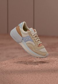 Beige and pastel-colored sneaker with suede and leather materials. Features a round toe, layered design, laces, and rubber sole.